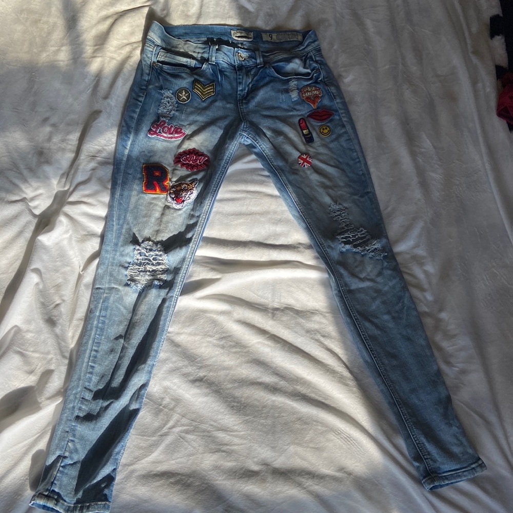 Light wash ripped jeans with patches and pin